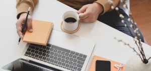 person holding white ceramic mug beside macbook pro